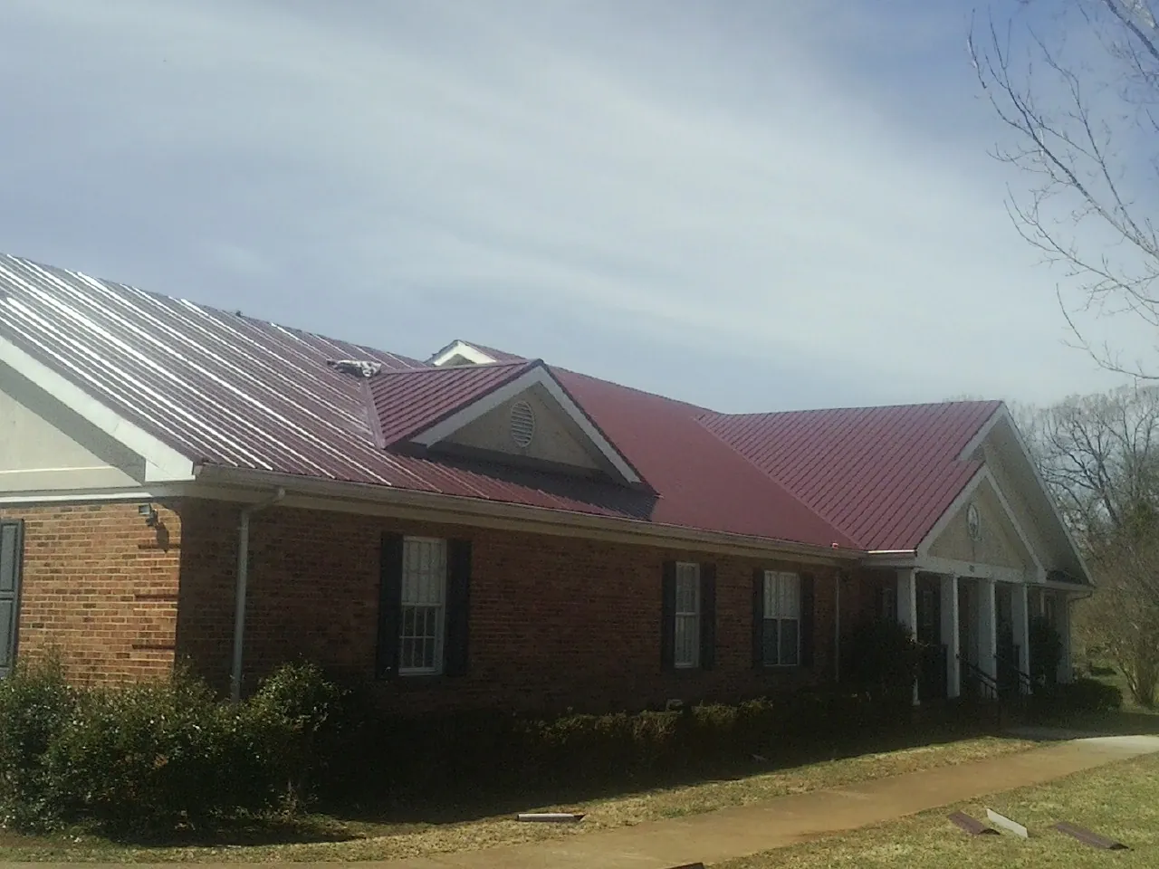 Red metal roof with gabled entries on a long brick building, from a Hail Damage Roof Repair job in Brownsville